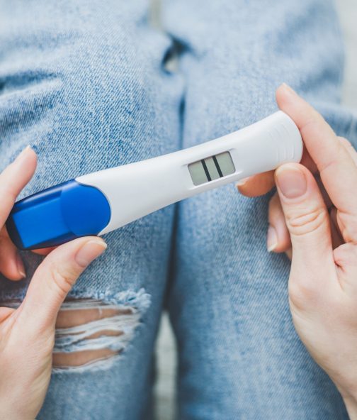 Woman looking on positive pregancy test Young woman hoding on jeans and looking on positive pregnancy test with two stripes. Lifestyle background. Pregnancy family concept. Horizontal.