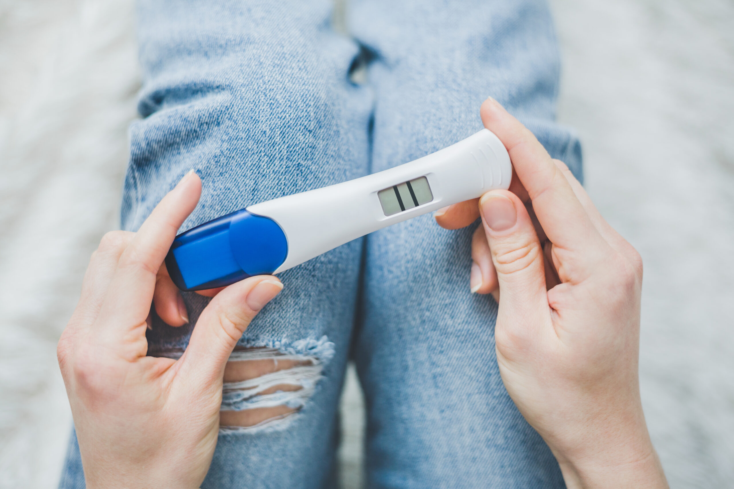 Young woman hoding on jeans and looking on positive pregnancy test with two stripes. Lifestyle background. Pregnancy family concept. Horizontal.